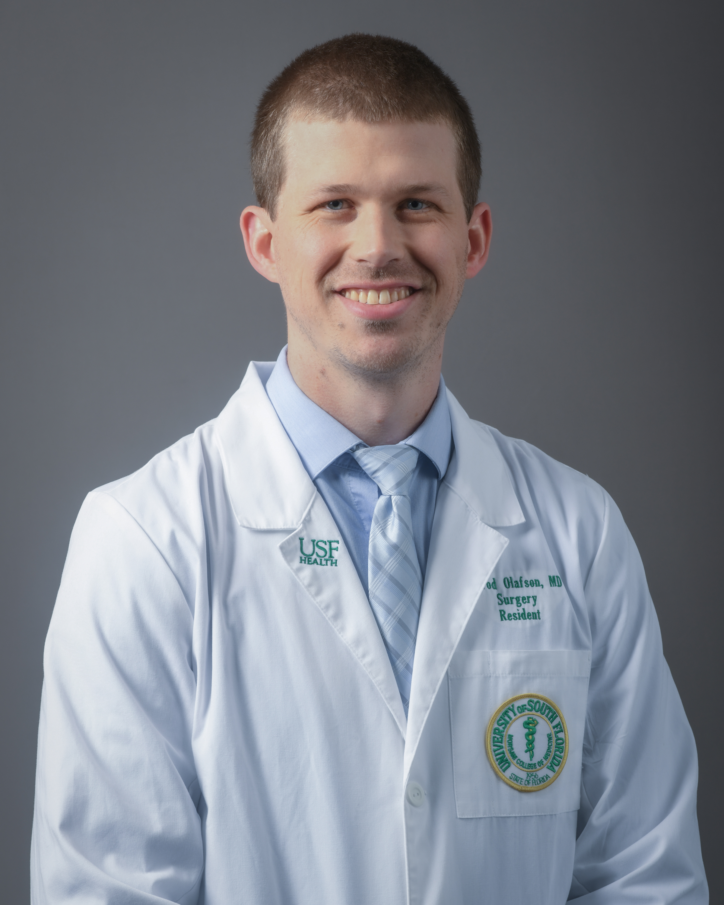 Headshot of Dr. Jarrod Olafson. He is wearing a white coat, light blue shirt, and blue/white tie. 