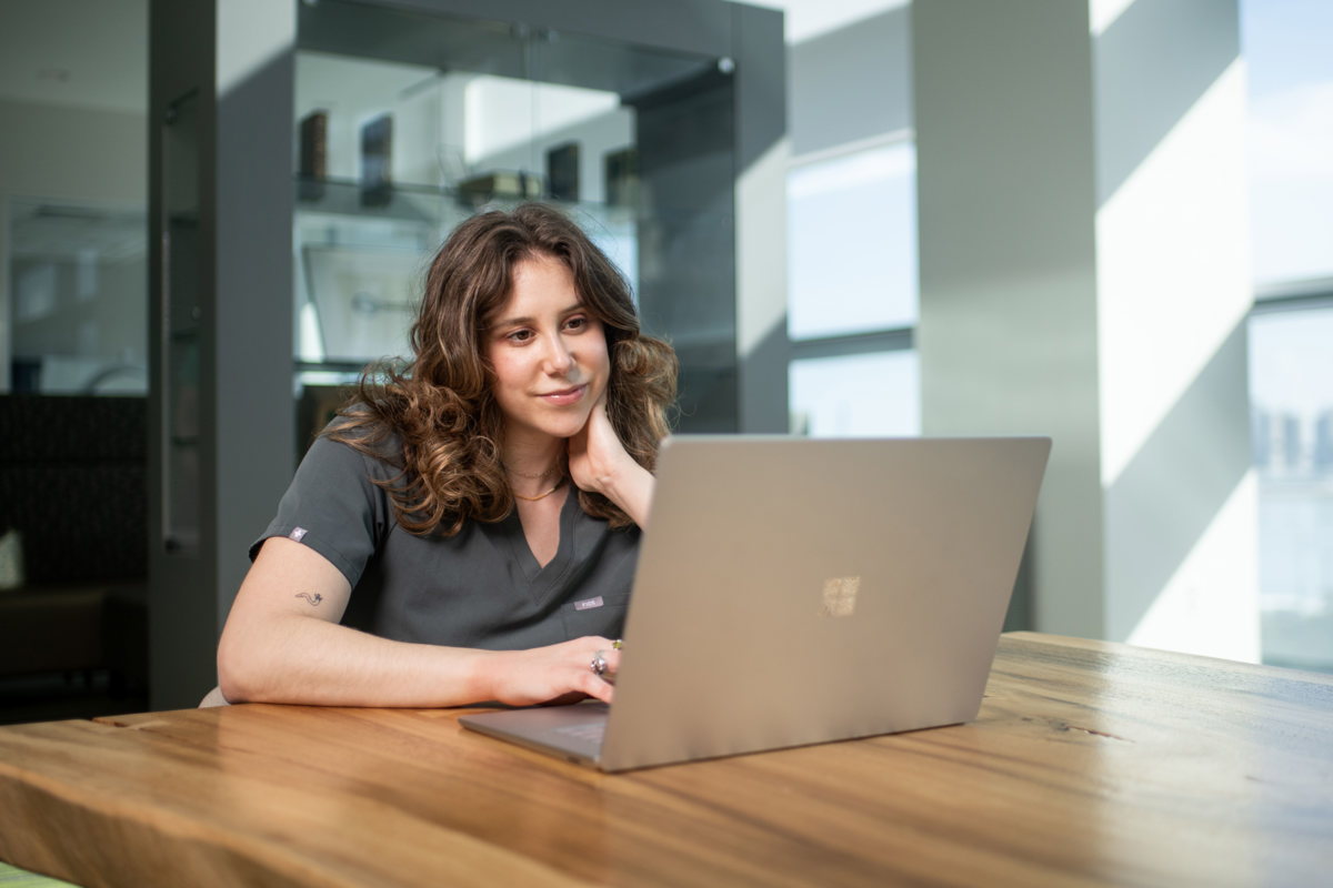 Student sitting at a table smiling at a computer