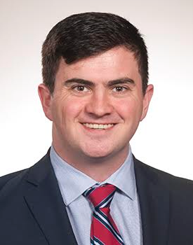 Headshot of Dr. Anderson with short dark hair, wearing a dark suit jacket, light blue shirt, and red striped tie against a white background.