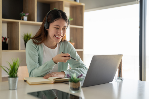 A woman smiling while looking at her laptop and wearing a headset