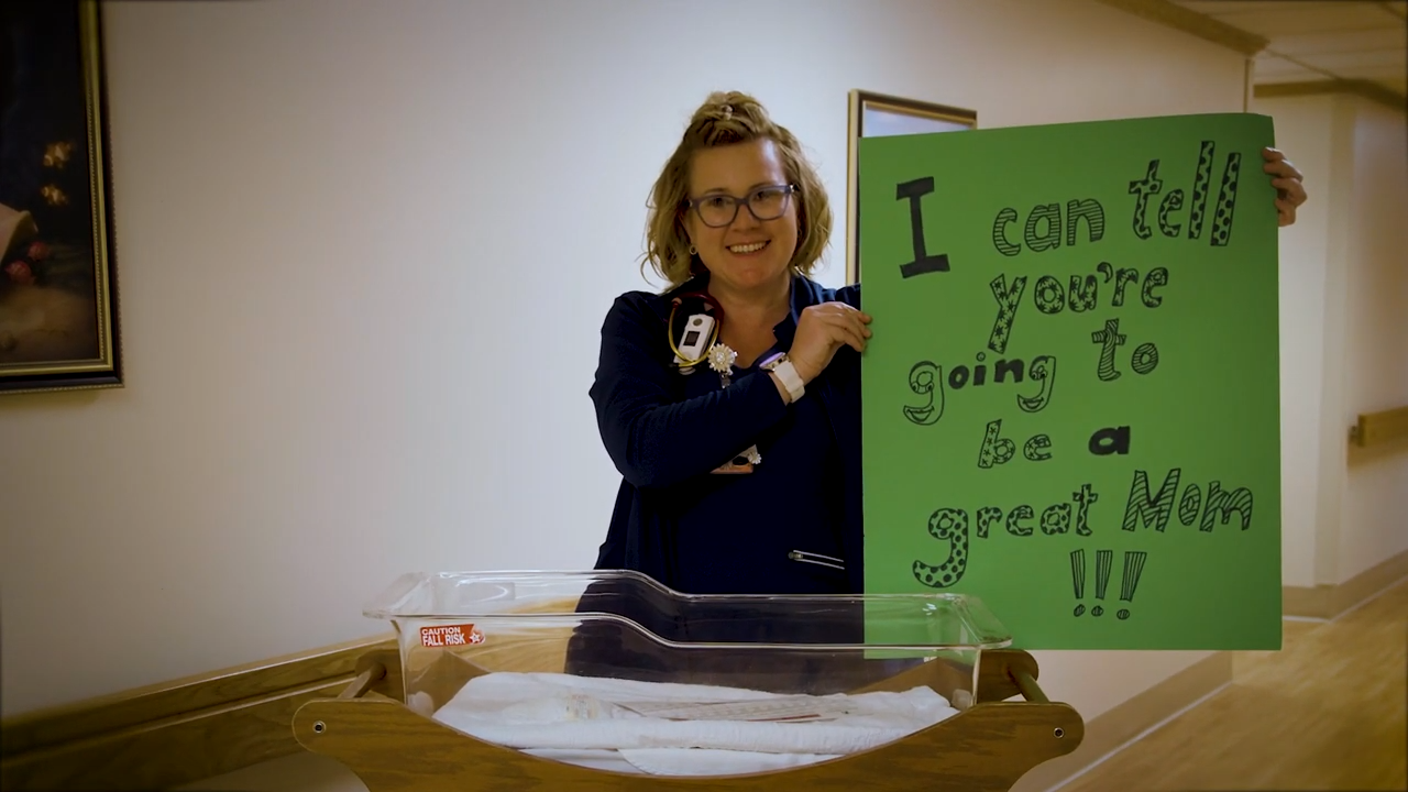 A woman holding a sign that says "I can tell you are going to be a great mom!!!"