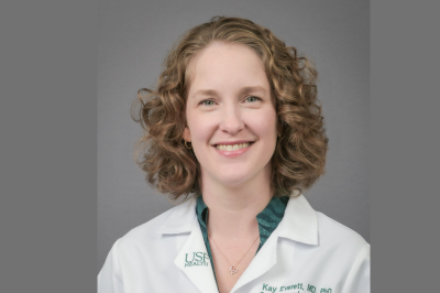 Dr. Kay Everett smiling wearing a USF medical white coat and a green blouse