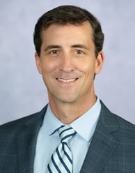 Benjamin Mackie headshot smiling with a blue suit and tie