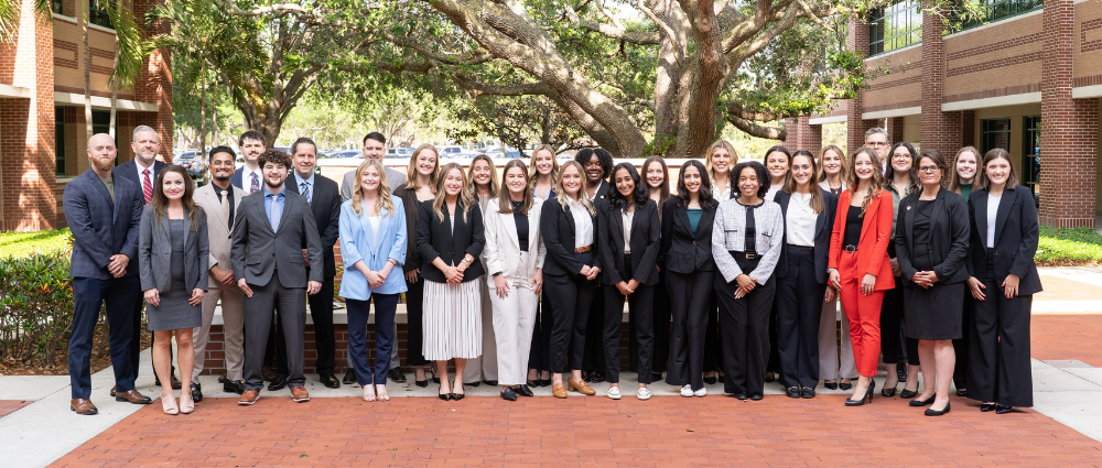 A group of MHA students and faculty standing together and posing for a photo in an outdoor courtyard setting