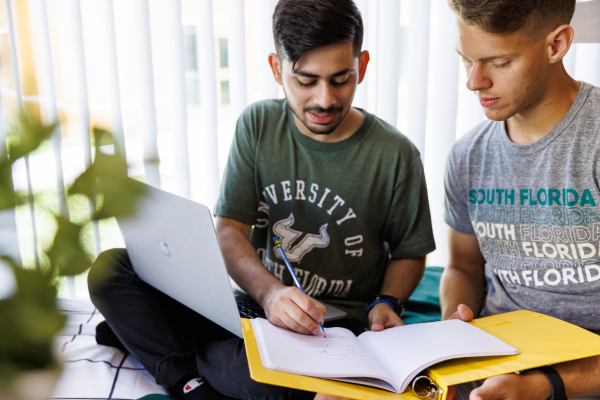 Two students studying at a table with notebooks and a laptop