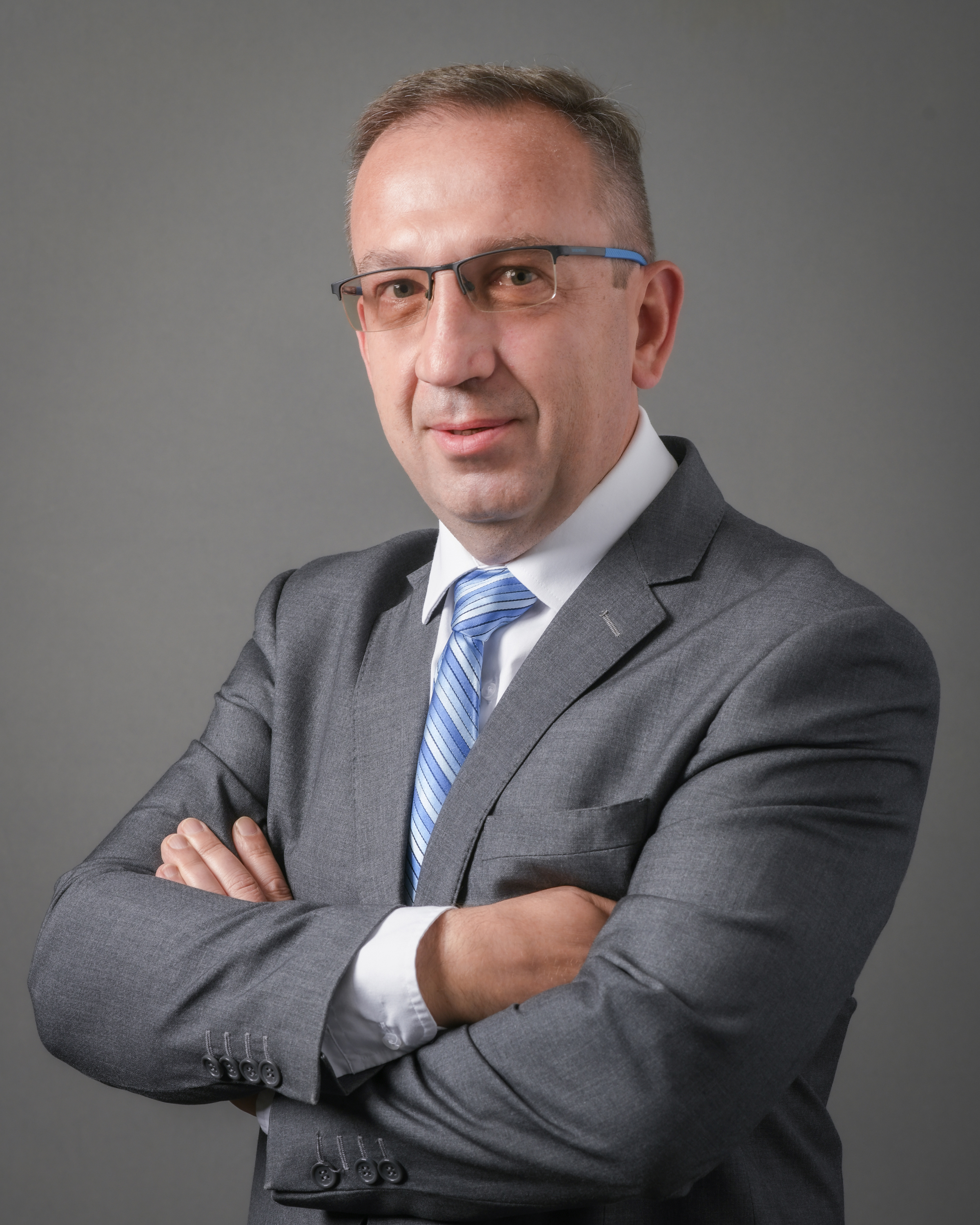 Dr. Staruschenko posing with  his arms crossed smiling in a grey suit with a blue striped tie