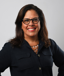 Monica Matos smiling, posing with hands on her hips, with wearing a black blouse