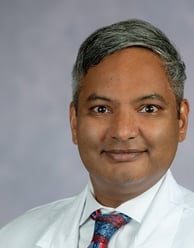 Kiran Dhanireddy headshot smiling with a white shirt wearing a blue and red tie