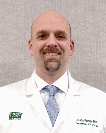 Dr Parker smiles wearing a USF Health medical white coat and blue tie