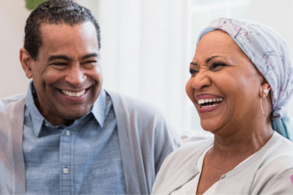 A smiling couple, with the woman wearing a colorful head scarf, radiating joy and warmth in a sunny setting.