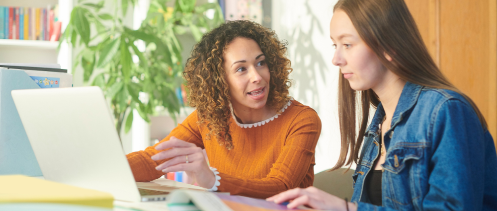 An advisor speaking with a student as they both look at a computer in an office setting