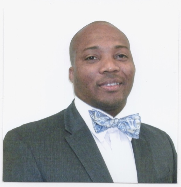 Dr McLean smiling wearing a grey suit with white dress shirt and blue bow tie, white background