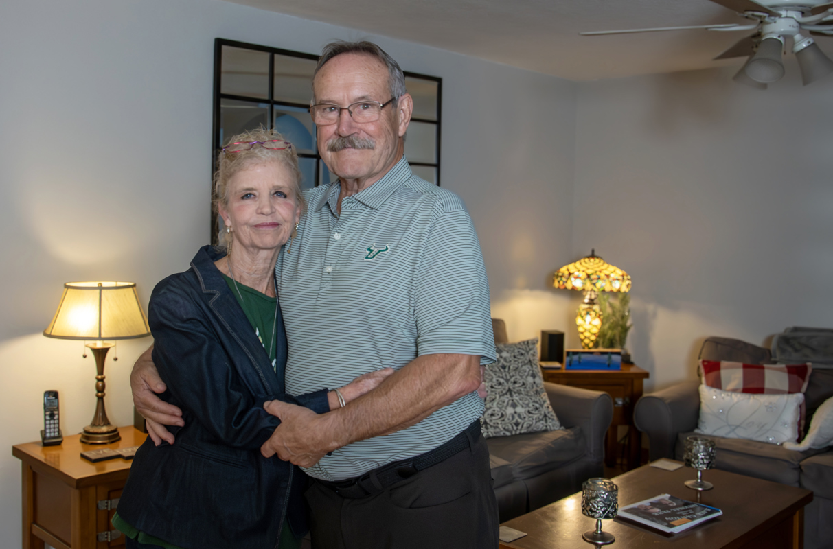Karen and Bob smiling and hugging one another in a living room
