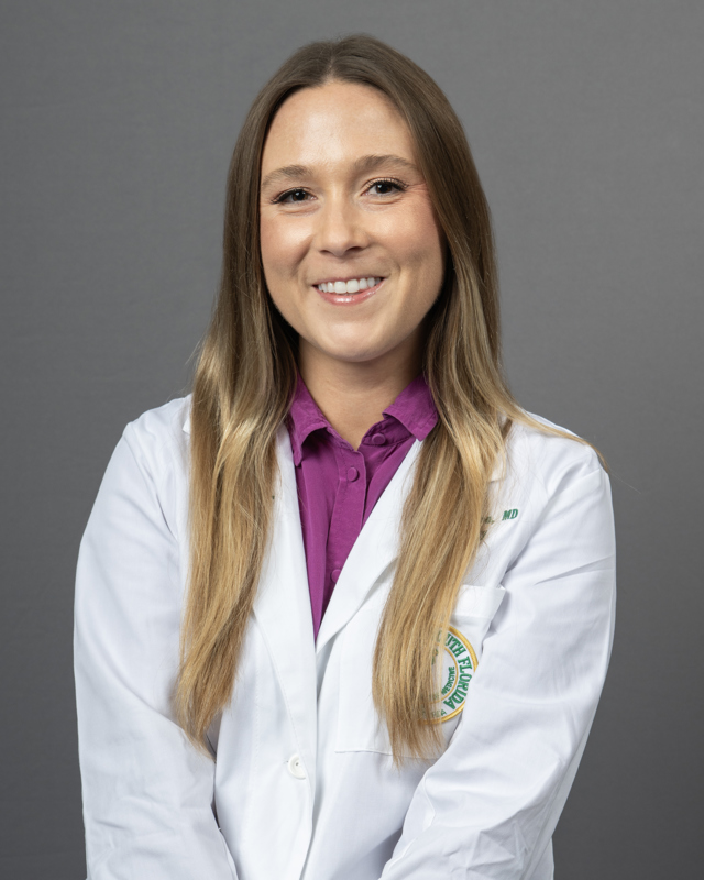 Chandler Johnson smiling wearing a pink blouse with a USF Health branded medical white coat