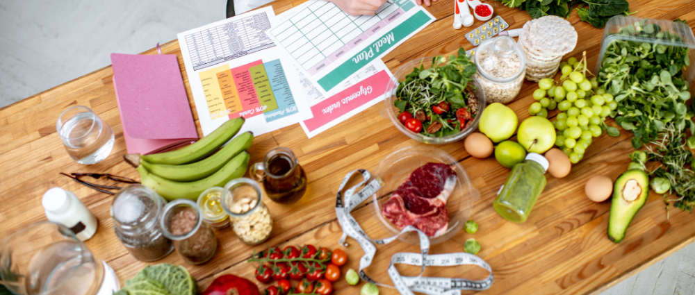 A person sitting at a table with a bunch of fruits and vegetables near them working on nutrition and wellness planning documents