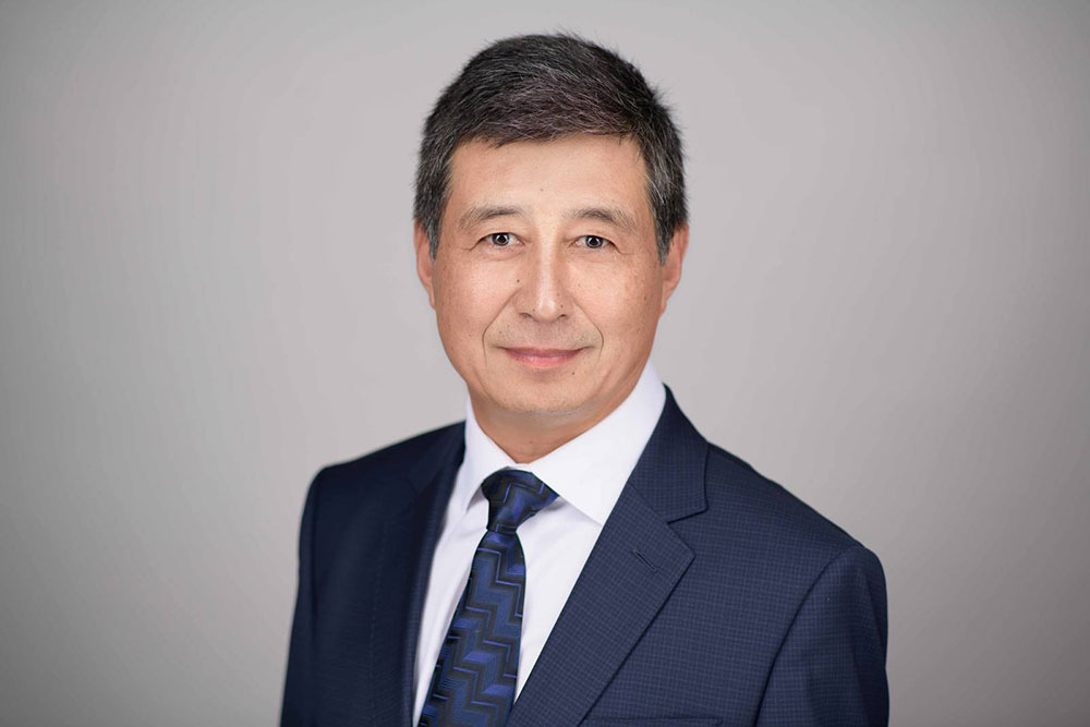Dr. Ruisheng Liu smiling for a headshot wearing a navy blue suit and tie with a white shirt