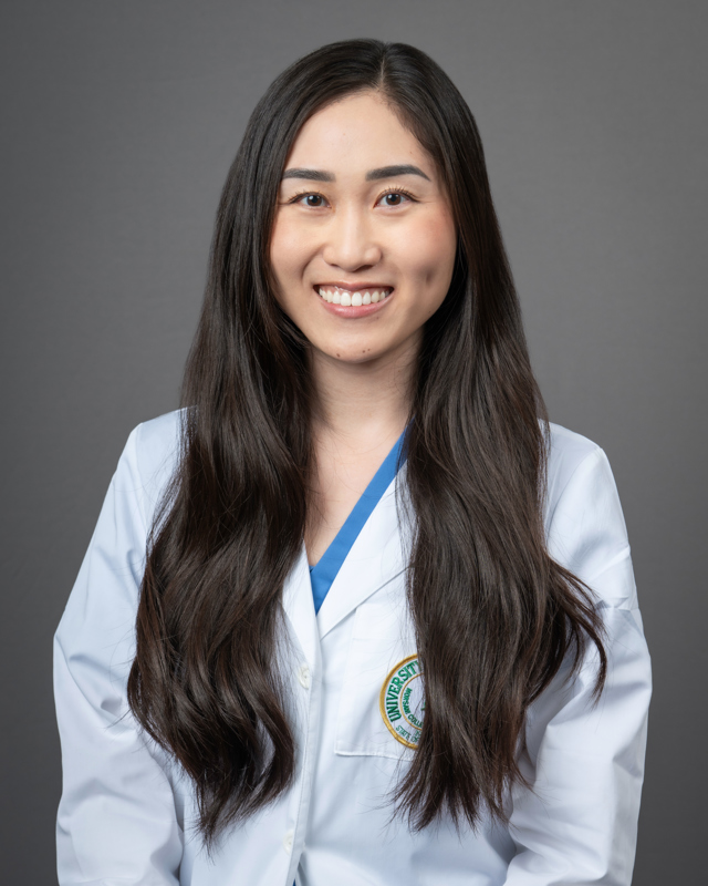 Adrianne Pan smiling wearing a USF Health braded medical white coat with a blue blouse