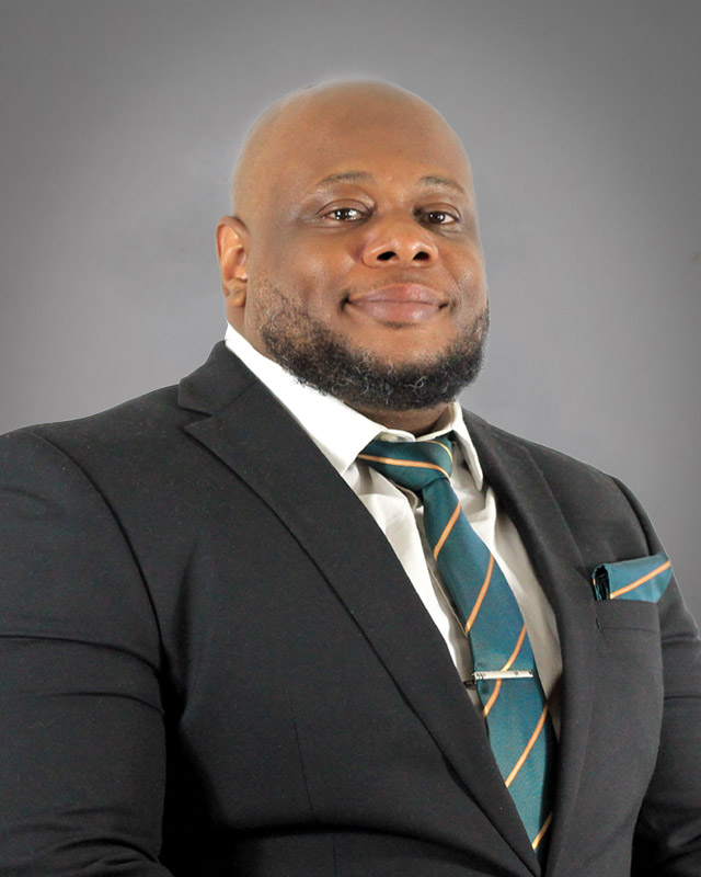 Dwayne Burtin smiling wearing a black suit with green and gold striped tie