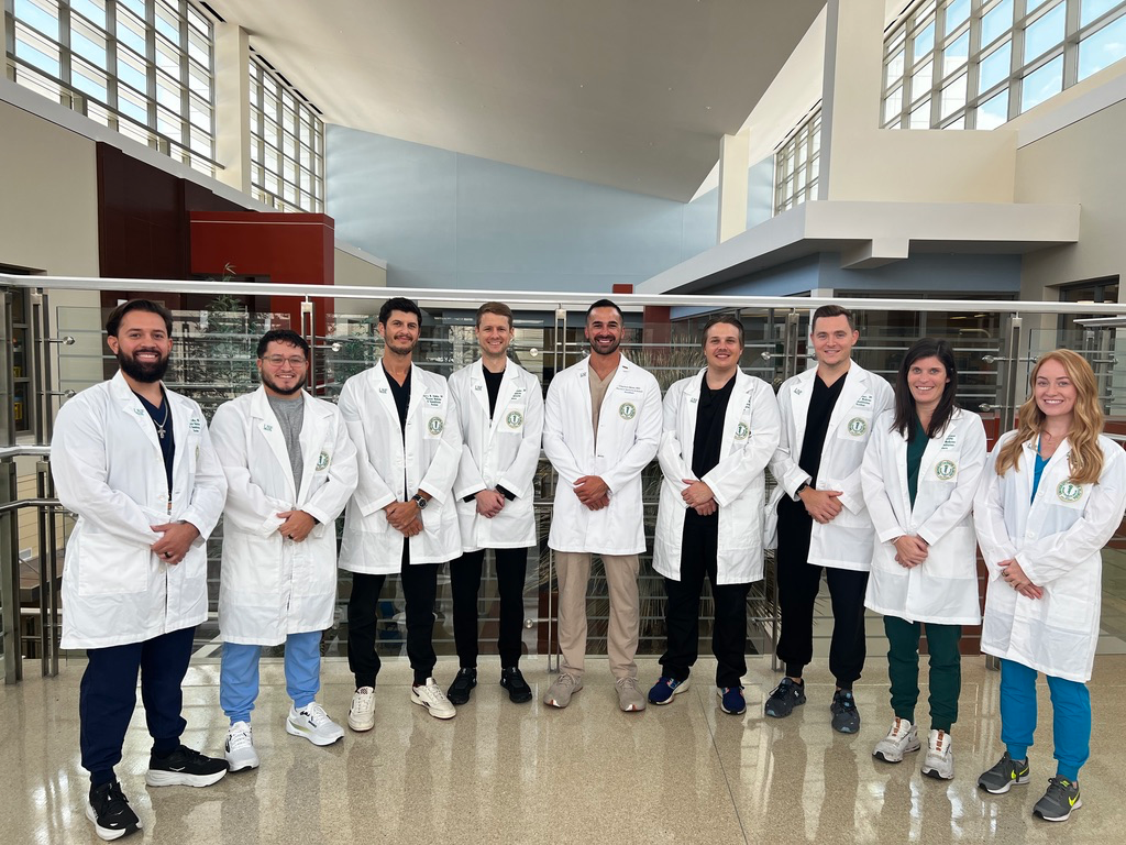 USF Health Neurology PMR residents standing in a semi-circle smiling wearing medical white coats