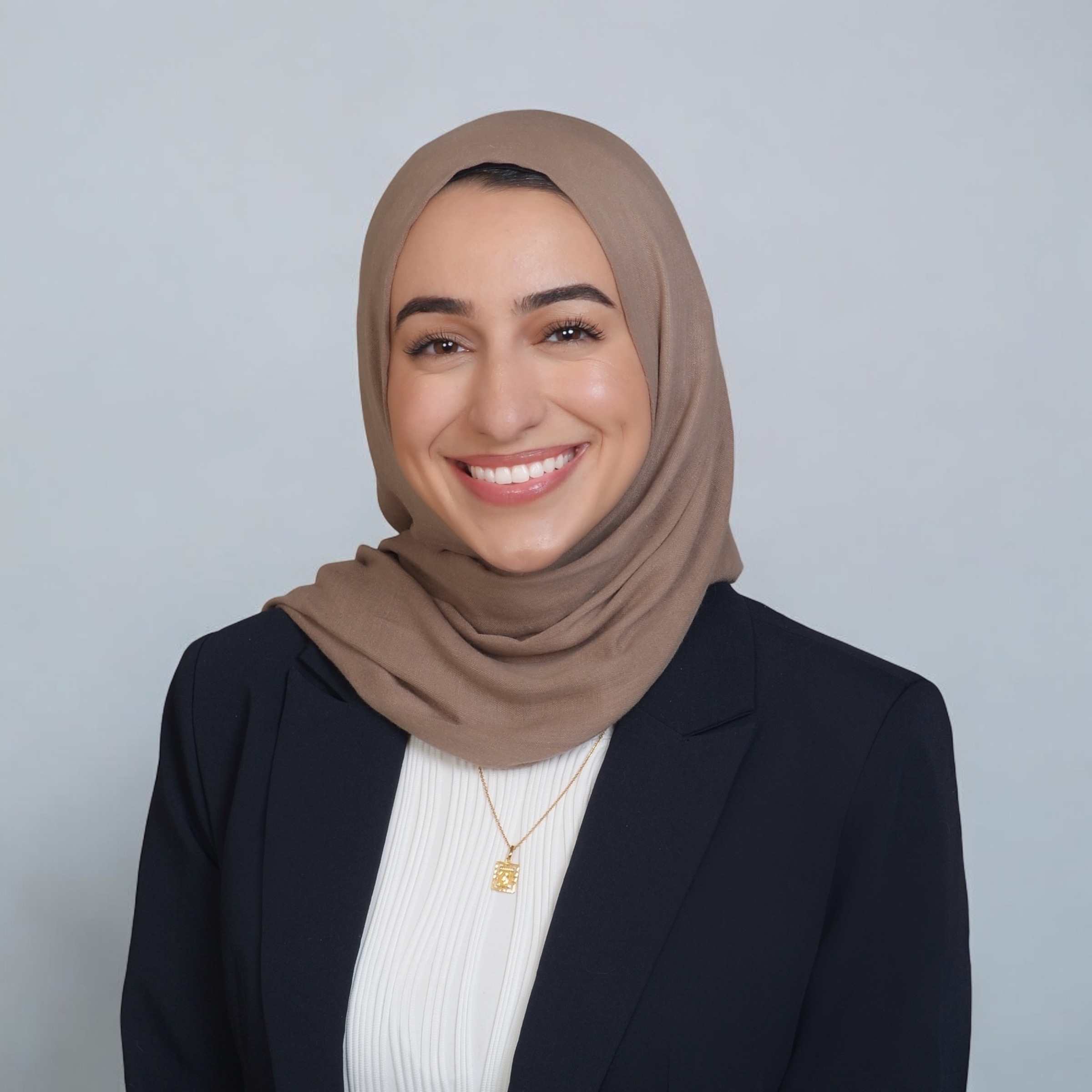 Malak Ibrahim smiling for a headshot wearing a brown hijab, white blouse and black blazer