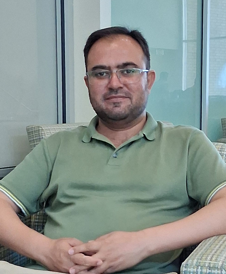 Basharat Hussain shitting in a chair wearing a sage green polo shirt wearing glasses