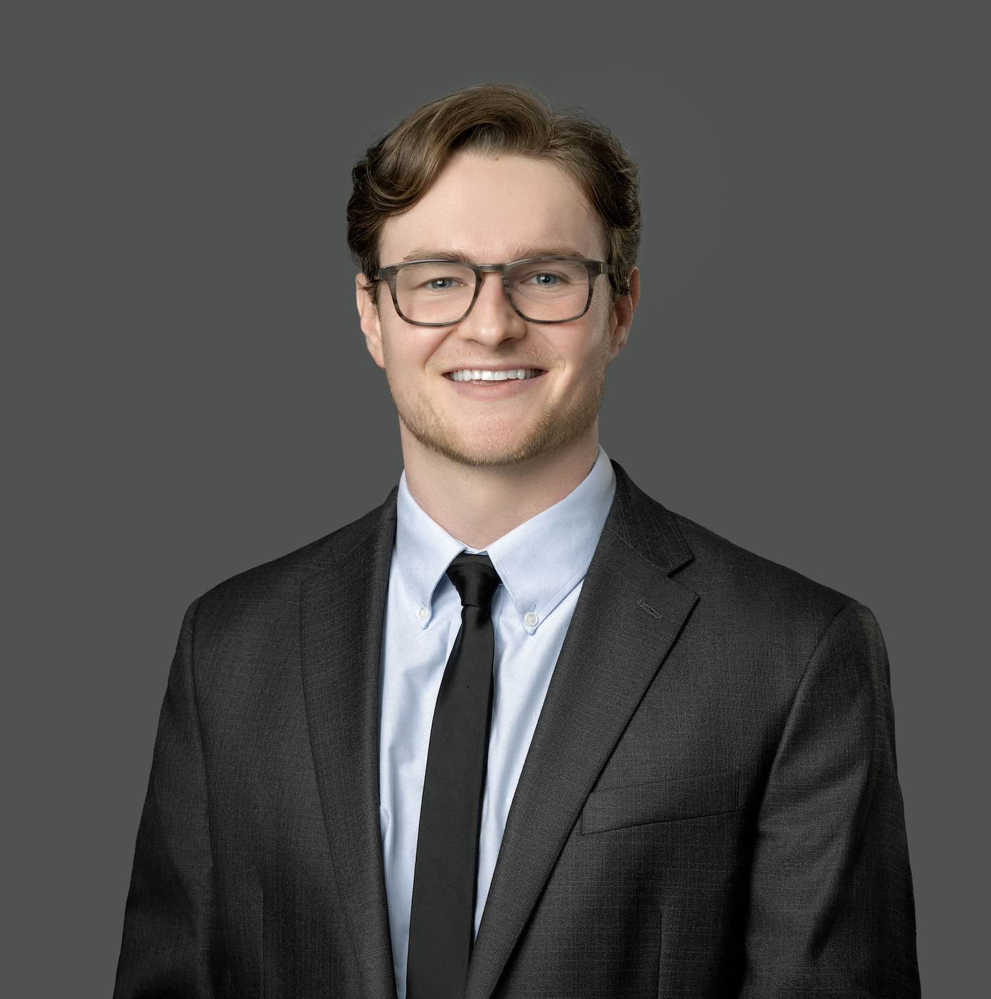 Zack Levine smiling for a headshot wearing a blur shirt and grey suit and tie