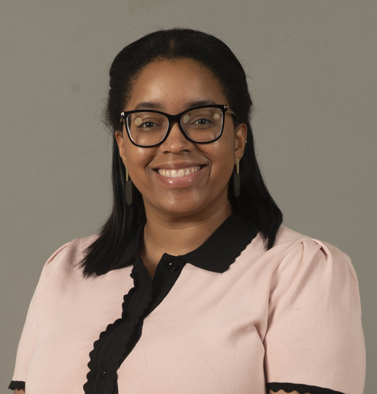 Chelsea Jones smiling wearing a pink and black blouse in front of a grey backdrop