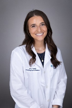 Amy smiling wearing a medical white coat with ling wavy brown hair