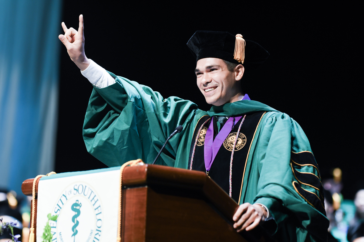 USF Health Morsani College of Medicine student at a podium signing "Bull" with fingers