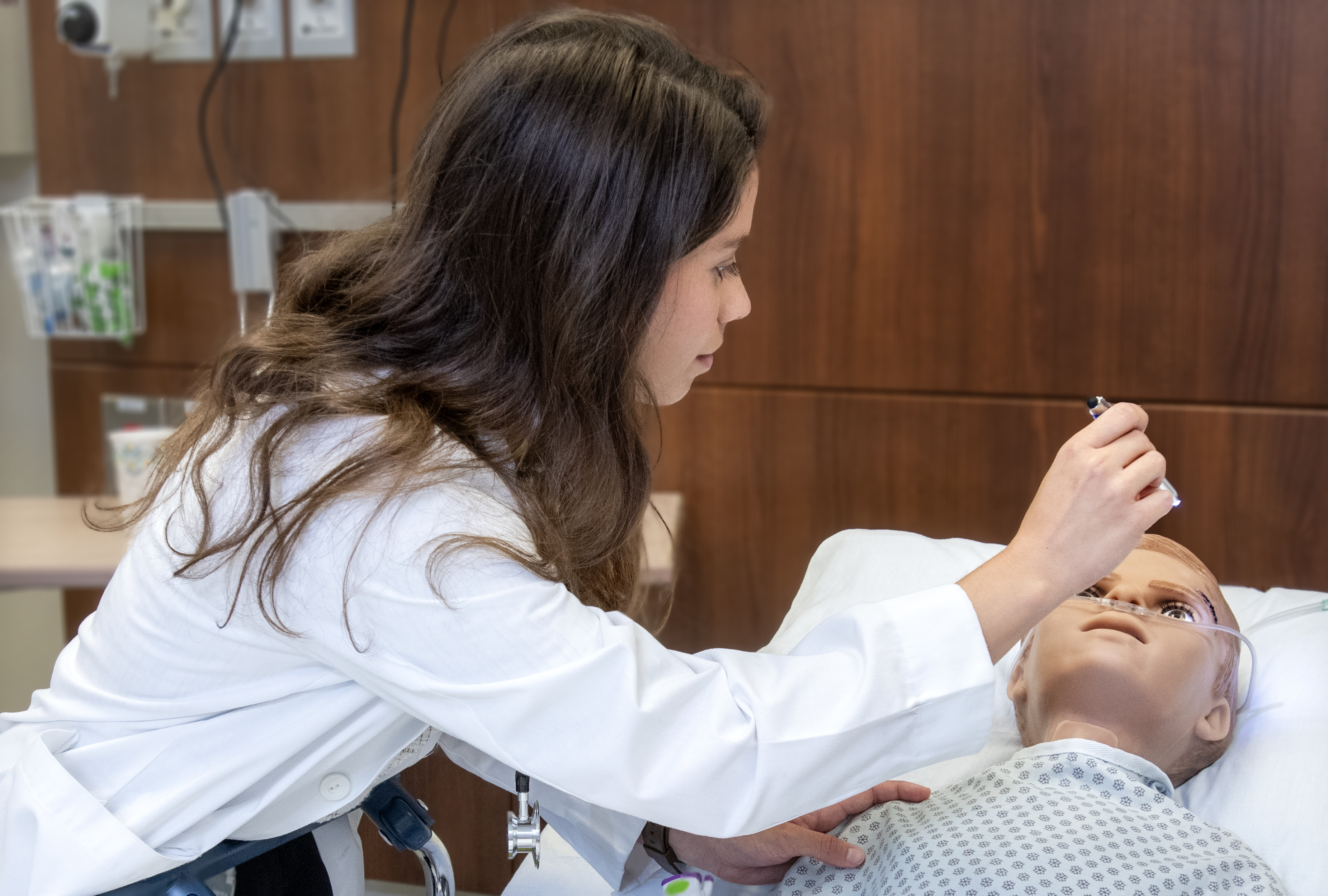 Student in medical white coat check the eyes of a mannequin patient