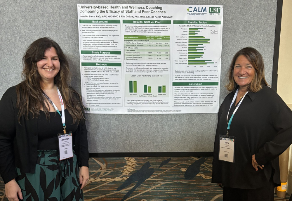 Two women stand together posing in front of a poster.