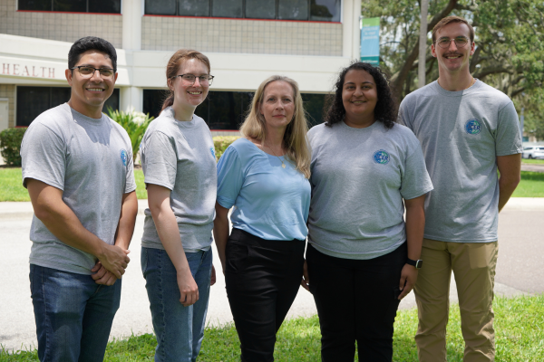 A group of volunteers and Dr. Christine McGuire-Wolfe standing together, posed in front of the COPH building
