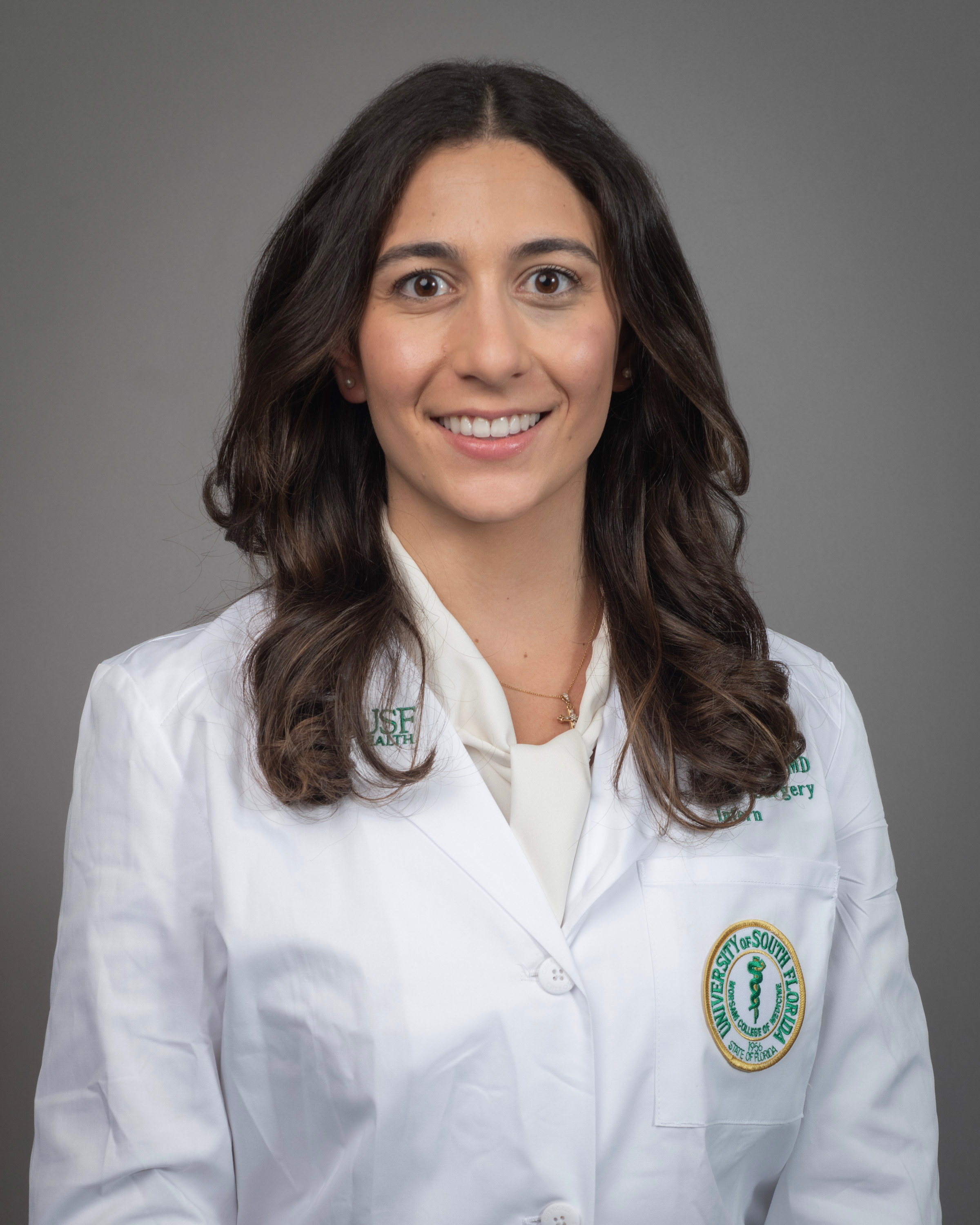 Christel smiling wearing a white blouse and wearing a USF Health branded medical white coat