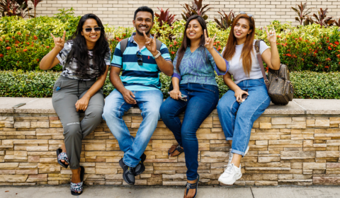 USF students sitting on a stone wall and holding up the "Go Bulls" hand symbol