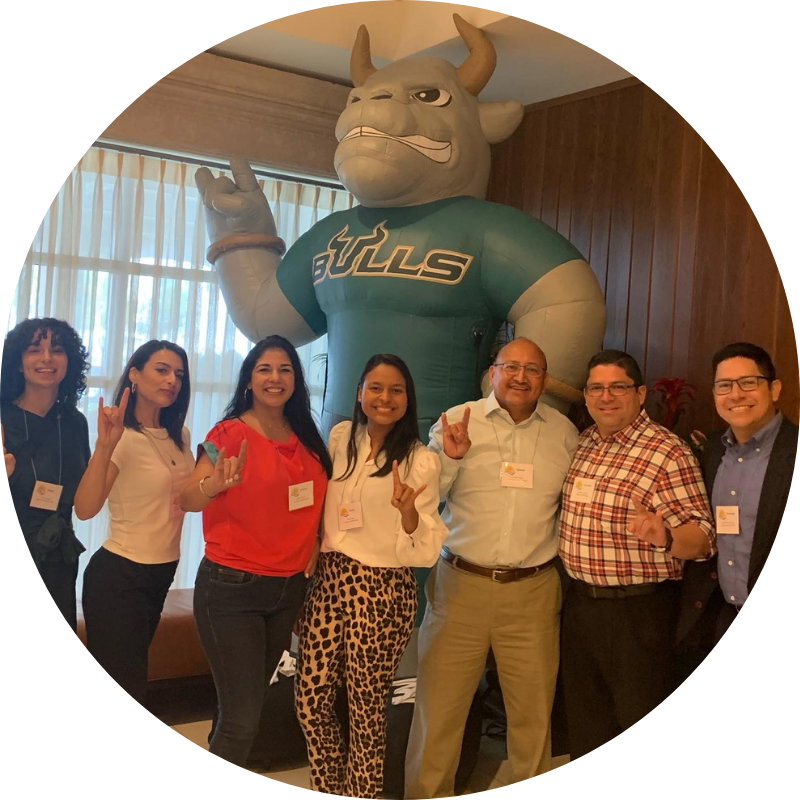 A group of people smiling for a photo and holding up the "Go Bulls" hand symbol
