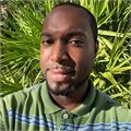 Neil Colman smiling wearing a green polo shirt with blue stripes standing in front of palm trees
