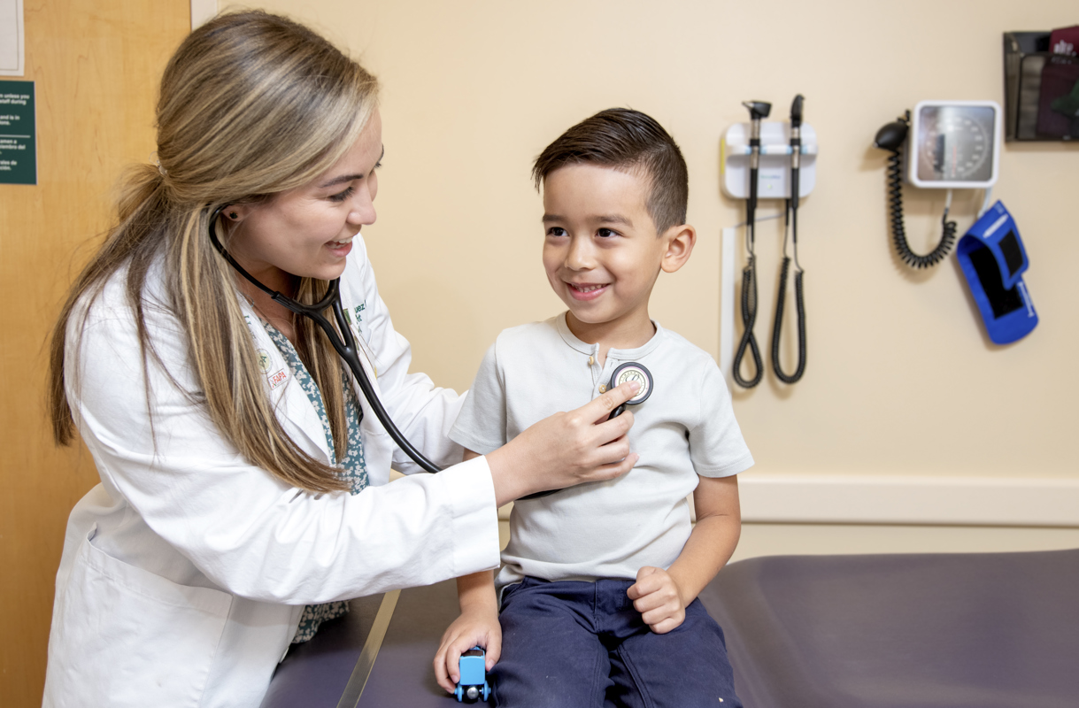 Physician Assistant checks a child sitting in a medical patient room with a stethoscope