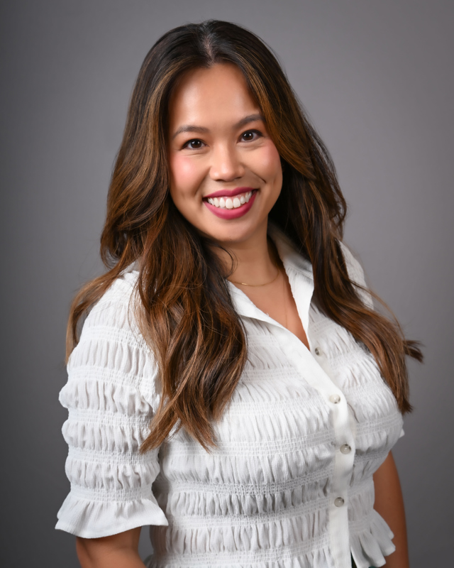 MyVan John smiling wearing a white blouse, standing at an angle in front of a grey backdrop