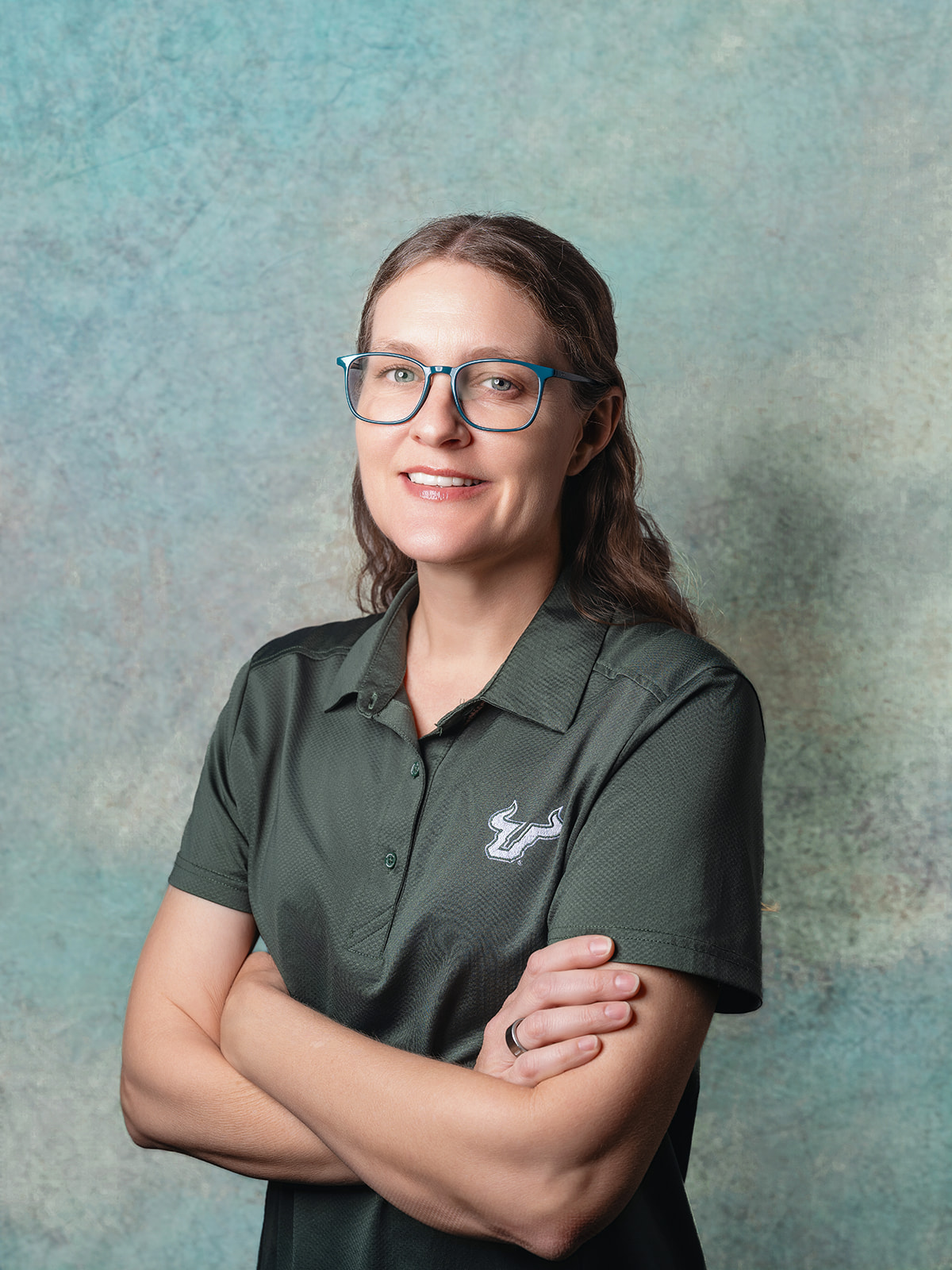 Jennifer O'Brien smiling with her arms crossed wearing a USF green polo shirt