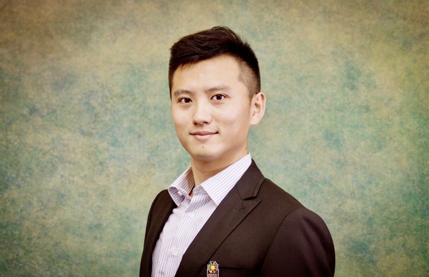 Hao Wang smiling wearing a burgundy jacket with a pink dress shirt