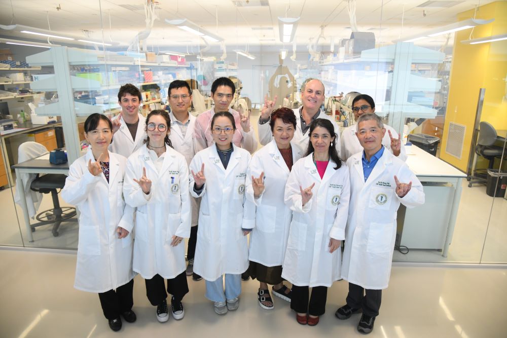 A group of medical professionals wearing white coats standing together in a medical lab, all people pictured and signing "bull" with their fingers, signaling the "Go Bulls" mantra of the University of South Florida 