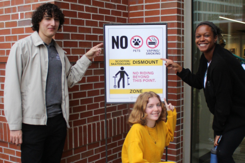 Three students pointing to a sign that says No Vaping/Smoking