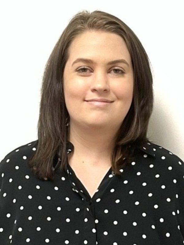 A headshot of Lauren Carns smiling in front of a white backdrop. She is wearing a black and white polka dot top.