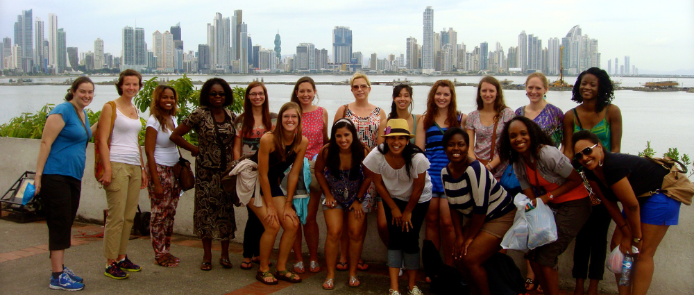 A group of students and faculty members in Panama for the Panama Program. They are standing in front of a body of water and the Panama skyline.