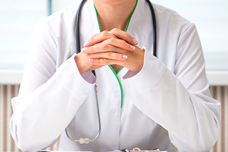Dr. is sitting at a desk with her hands together.