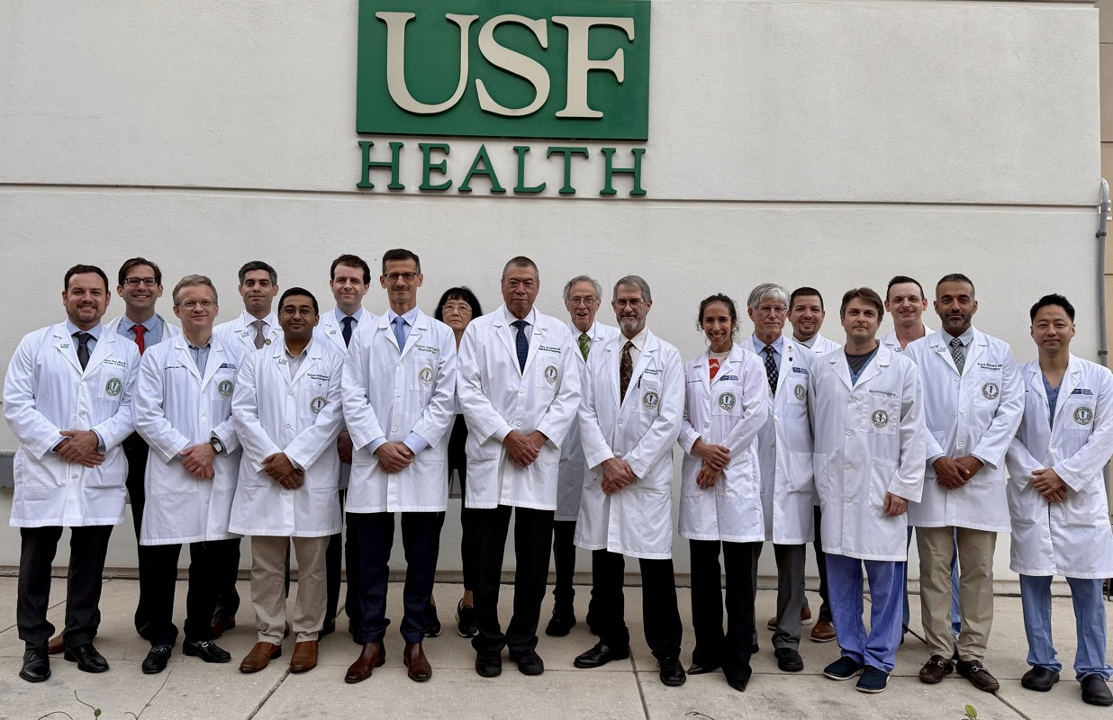 Neurosurgery physicians standing outside in lab coats in front of the USF Sign 