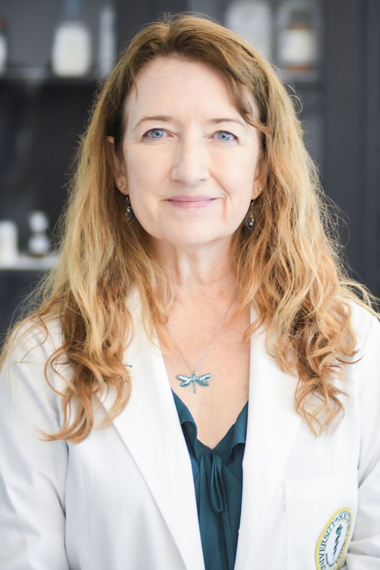 Laura Bohn smiling wearing a USF Health branded medical white coat with a green blouse