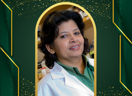 Dr. Subhra Mohapatra wearing a green shirt beneath a white lab coat in a green and gold background. 