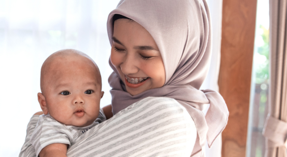 A mother in a hijab holding her baby and smiling