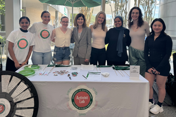 Volunteers from the Activist Lab stand at a white table, smiling and posing for a picture.